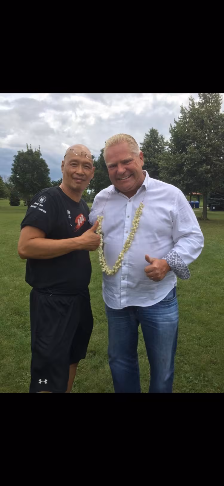 Sifu Sammy Cheng with a guest wearing a flower garland at an outdoor event