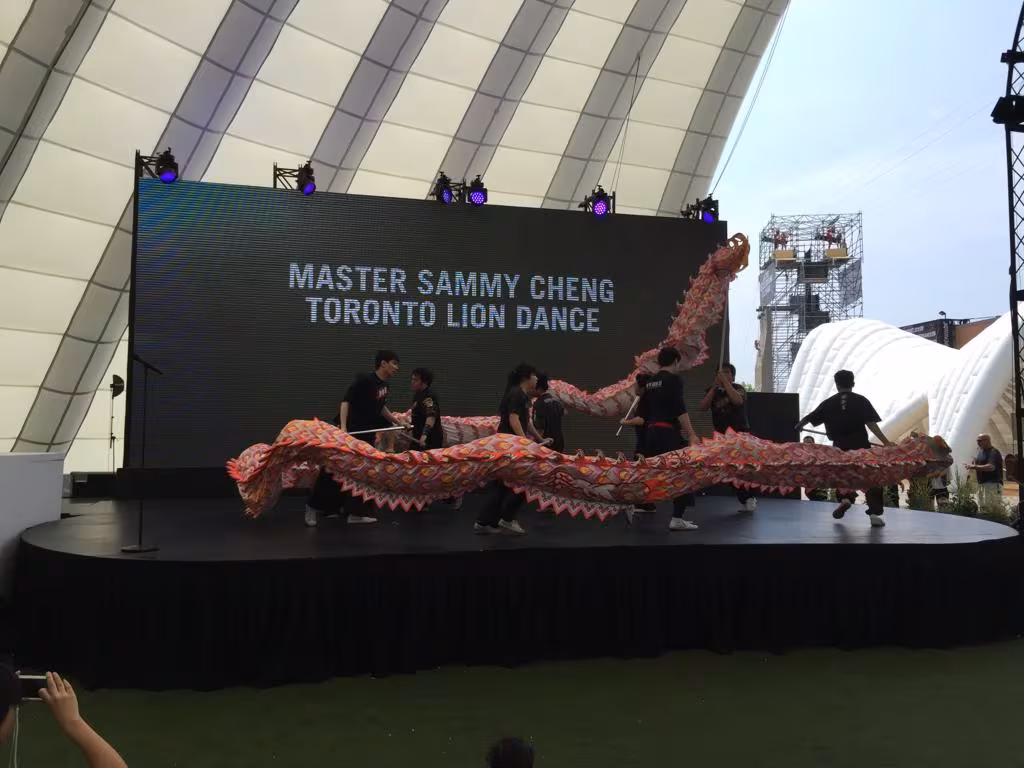 Dragon dance on an outdoor festival stage under a Master Sammy Cheng Toronto Lion Dance screen