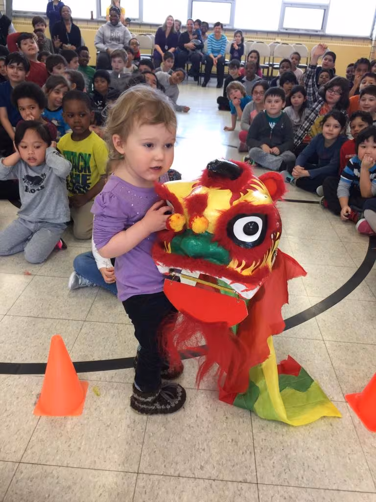 A young child playing with a small lion in a school gym full of students
